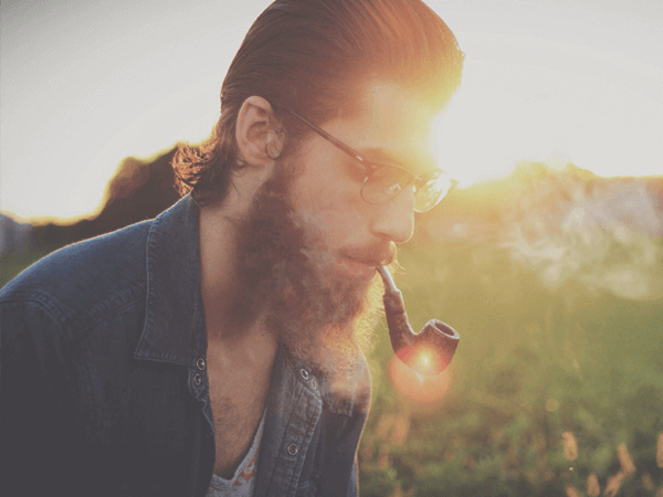 A hipster smoking a pipe in a field
